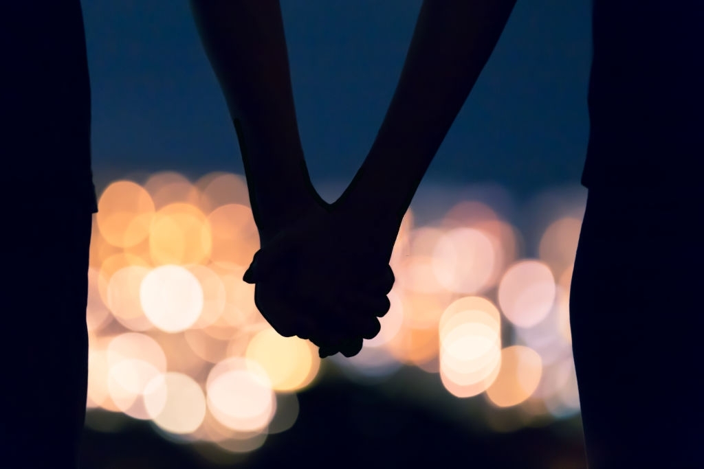 Couple holding hands against city night lights.